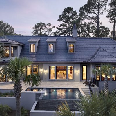Custom Home Design On Kiawah Island Featuring A Rear Exterior View With Large Windows, Disappearing-edge Pool, And Elevated Lowcountry Architecture By Marc Camens.