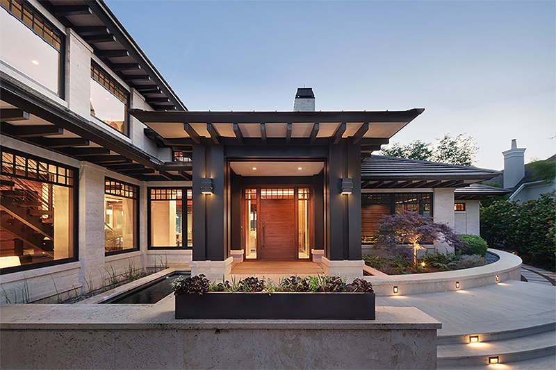 Evening view of a desert craftsman home with illuminated entry, strong architectural lines, and warm natural textures